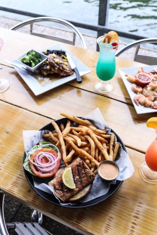 A plate of grilled fish with fries, lettuce, and onion, alongside colorful cocktails and a side of broccoli.