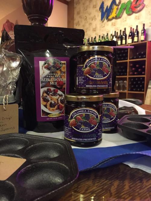 A display of cooking ingredients, including aebleskiver mix and jars of seedless preserves, set in a wine shop.