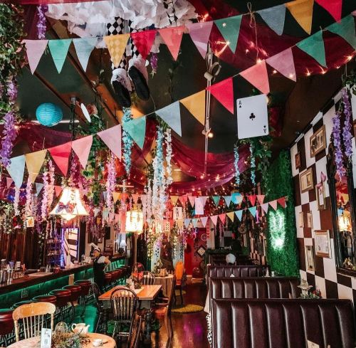 Colorful bunting and decorations hang from the ceiling of a vibrant, whimsical restaurant with cozy seating.