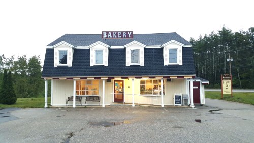 A charming bakery with a sign reading "BAKERY" on a two-story building, surrounded by trees and a parking area.