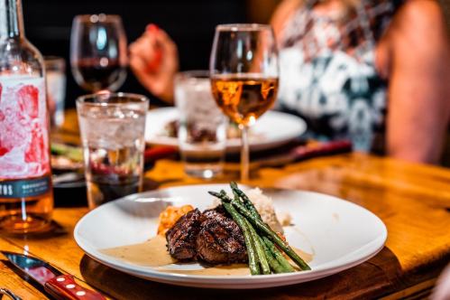 A plate of grilled steak with asparagus and rice, accompanied by glasses of wine and water on a wooden table.