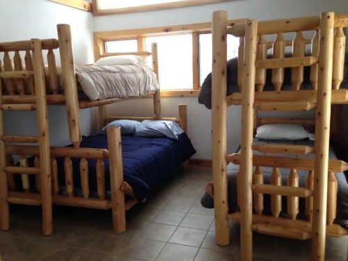 A cozy room with two wooden bunk beds and a single bed, featuring natural wood finishes and large windows.