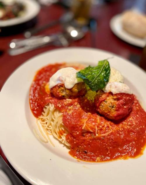 A plate of spaghetti topped with meatballs, marinara sauce, and a dollop of creamy sauce, garnished with a basil leaf.