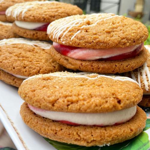 Close-up of golden cookies filled with cream and slices of fruit, arranged neatly on a platter.