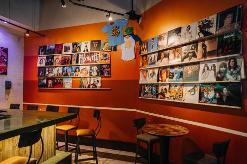 A cozy room with orange walls displaying vinyl records and T-shirts, featuring a bar with stools.