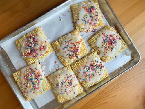 A tray of frosted pastries topped with colorful sprinkles, arranged neatly on parchment paper.