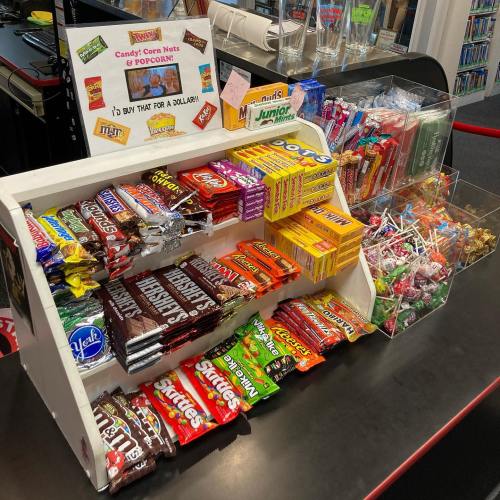 A display of various candies and popcorn for sale, with colorful packaging and a sign promoting $1 items.