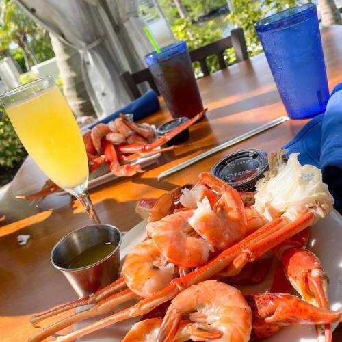 A table set with shrimp, drinks, and a small bowl of dipping sauce, surrounded by greenery.