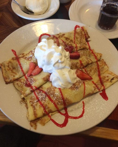 A plate of crepes topped with whipped cream, strawberries, and a drizzle of red sauce, served with a side of ice cream.