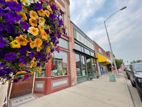 A charming street scene featuring colorful flower baskets, shops, and a cloudy sky.