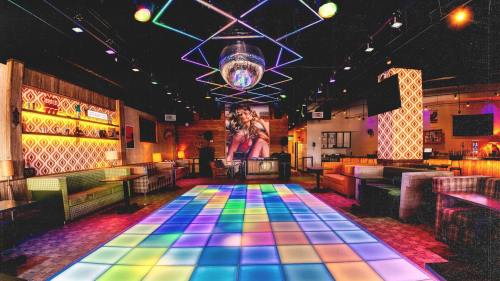 A vibrant dance floor with colorful lights, a disco ball, and retro decor in a lively nightclub setting.