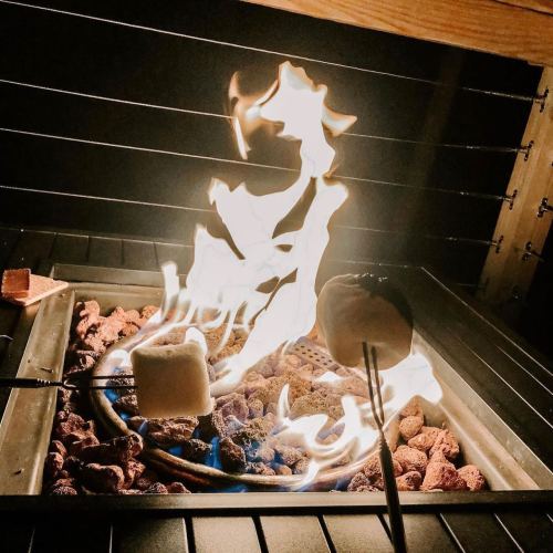 A close-up of marshmallows roasting over a fire, with flames dancing above a bed of glowing embers.