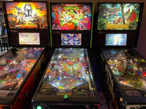 Three pinball machines featuring themes from "Mandalorian," "Teenage Mutant Ninja Turtles," and "Jurassic Park."