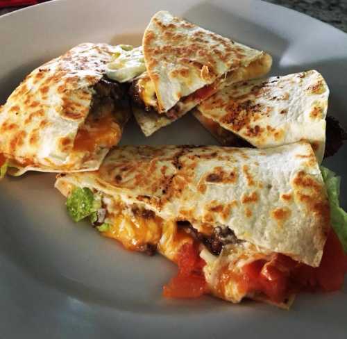 A plate of golden-brown quesadillas filled with cheese, lettuce, and tomatoes, cut into wedges.