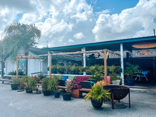 A colorful outdoor seating area with plants and furniture, under a blue sky with fluffy clouds.