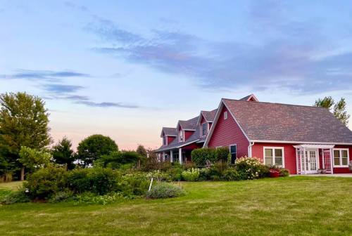 A red house with a sloped roof surrounded by greenery and flowers, set against a colorful sky at dusk.
