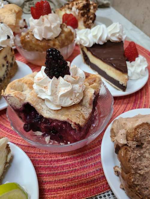 A variety of desserts including pies and cakes, topped with whipped cream and fresh berries, arranged on a colorful tablecloth.