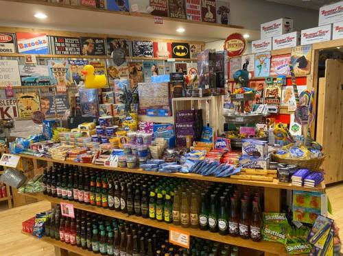 A colorful display of snacks, drinks, and novelty items in a shop, surrounded by various signs and decorations.