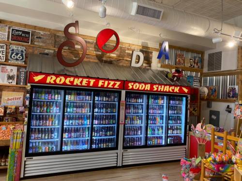 A colorful soda display at Rocket Fizz Soda Shack, featuring various soda bottles and a rustic wooden backdrop.