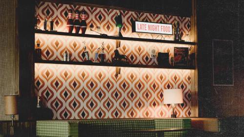 A retro-style bar shelf with drinks and snacks, illuminated against a patterned wall, labeled "Late Night Food."