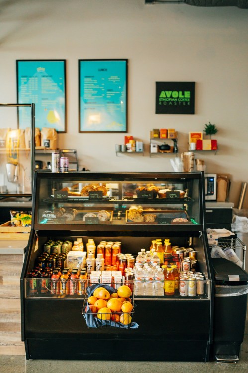 A display fridge filled with drinks and snacks, surrounded by a cozy café atmosphere with menu boards on the wall.