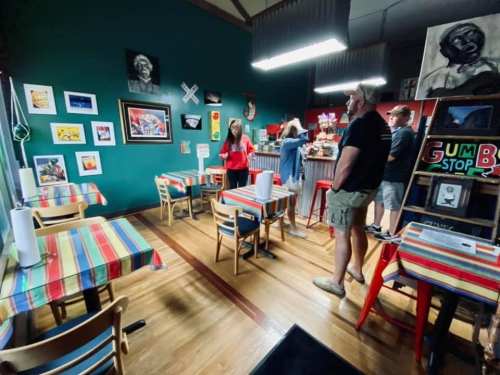 A colorful restaurant interior with striped tables, artwork on the walls, and customers at the counter.