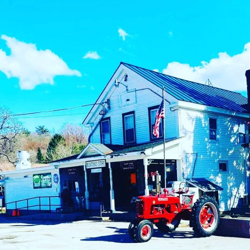 A red tractor parked in front of a white building with a flag, under a blue sky with scattered clouds.
