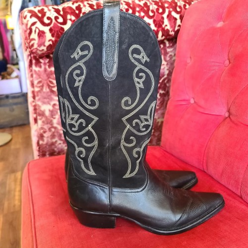 A black cowboy boot with intricate silver stitching, resting on a red upholstered chair.
