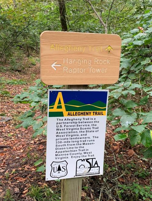Sign for the Allegheny Trail, pointing to Hanging Rock and Raptor Tower, surrounded by greenery.