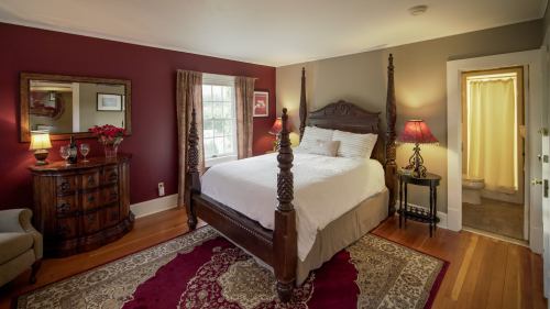 Cozy bedroom with a four-poster bed, warm lighting, a decorative rug, and an adjoining bathroom.