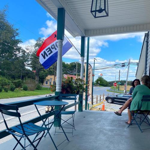 A porch with two chairs, a "OPEN" flag waving, and a view of a road and trees under a blue sky.