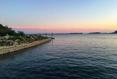 A serene waterfront view at sunset, with calm waters and a distant shoreline under a colorful sky.