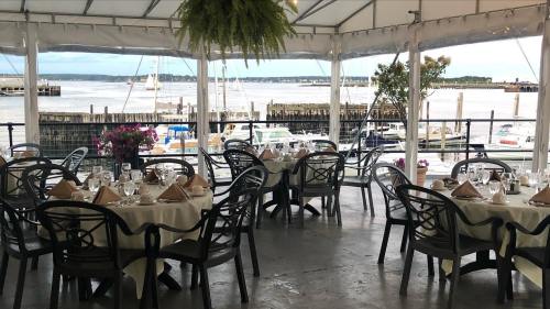 A waterfront dining area with tables set for a meal, featuring a view of boats and a harbor through a tent.