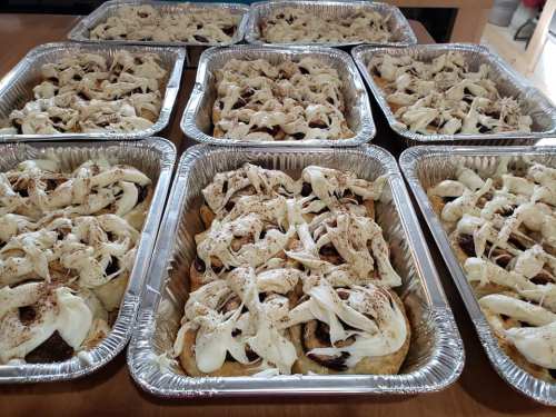 Several aluminum trays filled with layered dishes topped with white mushrooms and seasoning.