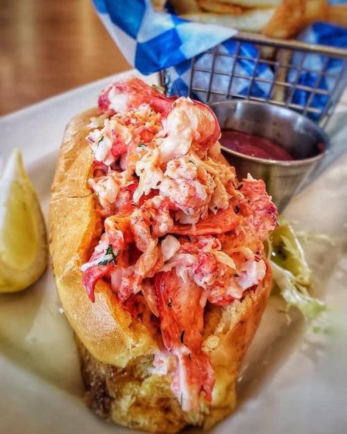 A lobster roll filled with fresh lobster meat, served with a side of fries and a small cup of dipping sauce.