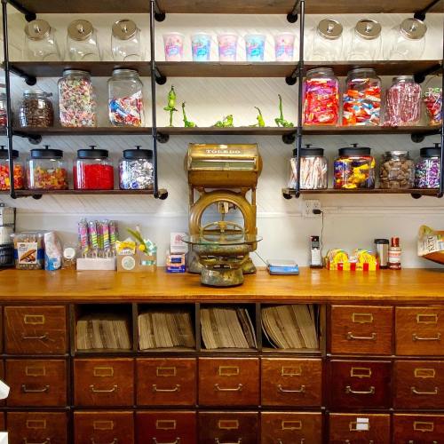 A colorful candy shop display with jars of sweets on shelves and a wooden counter with drawers.