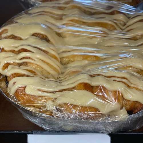 A close-up of a cinnamon roll topped with creamy icing, placed on a dark surface.