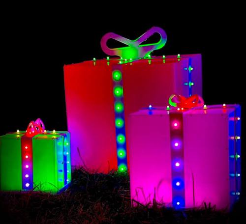 Three brightly lit, oversized gift boxes in red, green, and pink, set against a dark background.