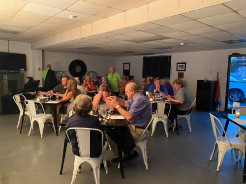A group of people dining together in a casual setting, with tables and chairs arranged in a well-lit room.