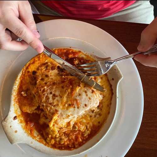 A close-up of a cheesy baked dish on a plate, with a fork and knife ready to serve.