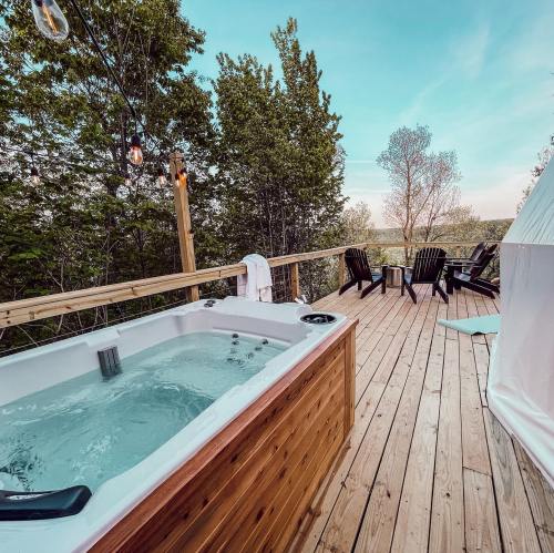 A wooden deck with a hot tub, surrounded by trees and a scenic view, featuring outdoor chairs and soft lighting.