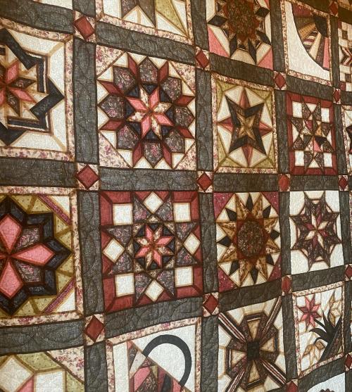 A colorful quilt featuring a patchwork of intricate star patterns in various shades of red, pink, and gold.