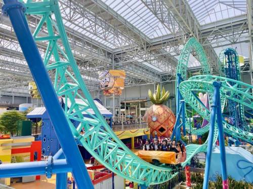 A colorful indoor amusement park featuring a roller coaster and a large pineapple structure.