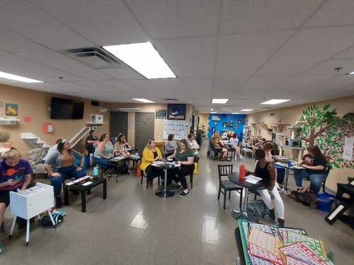 A classroom filled with students seated at tables, engaged in activities, with colorful decorations on the walls.