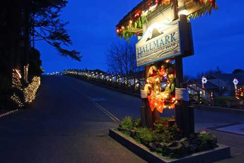 A festive street sign adorned with holiday decorations, leading up a gently sloping road illuminated by lights at dusk.