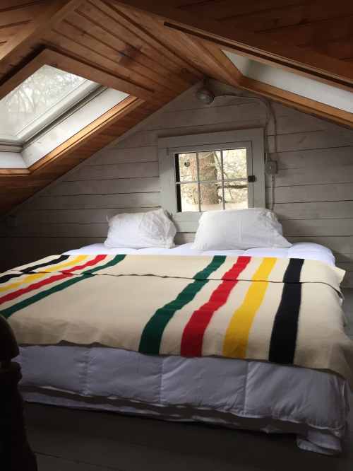 Cozy attic bedroom with a sloped wooden ceiling, two white pillows, and a colorful striped blanket on the bed.