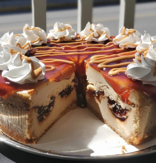 A sliced cheesecake topped with whipped cream and caramel drizzle, revealing a rich filling with a dark layer inside.