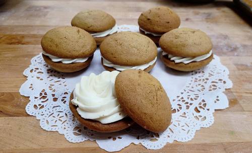 A plate of six whoopie pies with creamy filling, arranged on a decorative lace doily.
