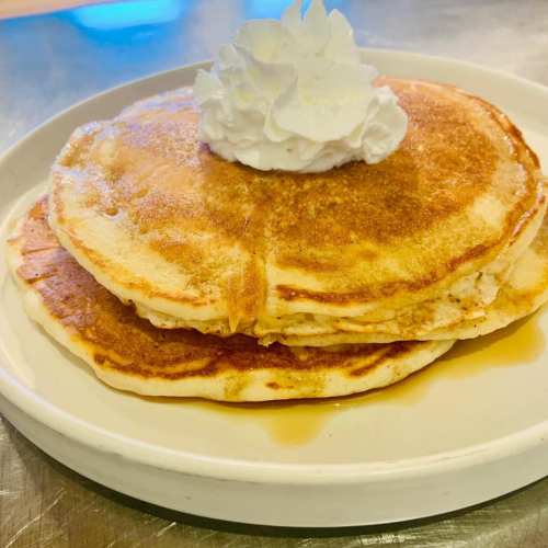 Two fluffy pancakes stacked on a plate, topped with a dollop of whipped cream.