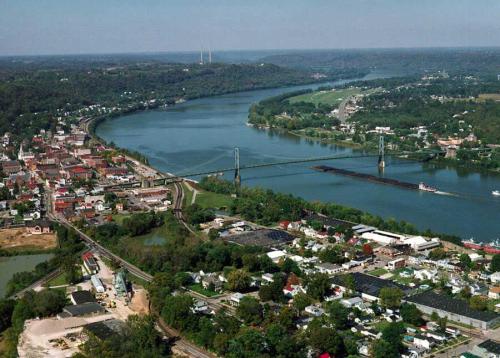Aerial view of a river town with a bridge, lush greenery, and a mix of residential and commercial buildings.